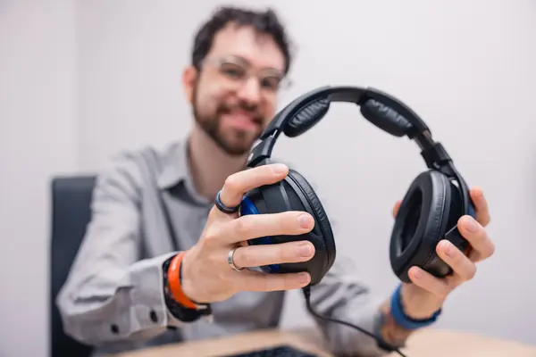 Mann hält große Over-Ear-Kopfhörer für Audio-Test im Büro in die Kamera