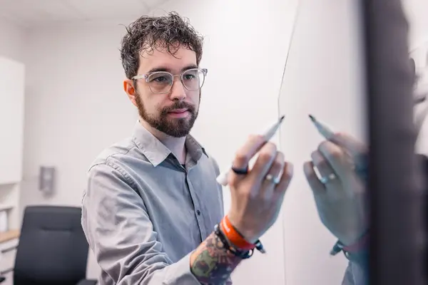 Mann im Büro schreibt mit Stift auf Whiteboard, Meeting und Strategieplanung