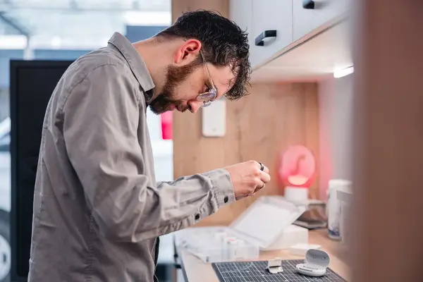 Mann mit Schutzbrille prüft Bauteil in Werkstatt, Elektronik-Reparatur.