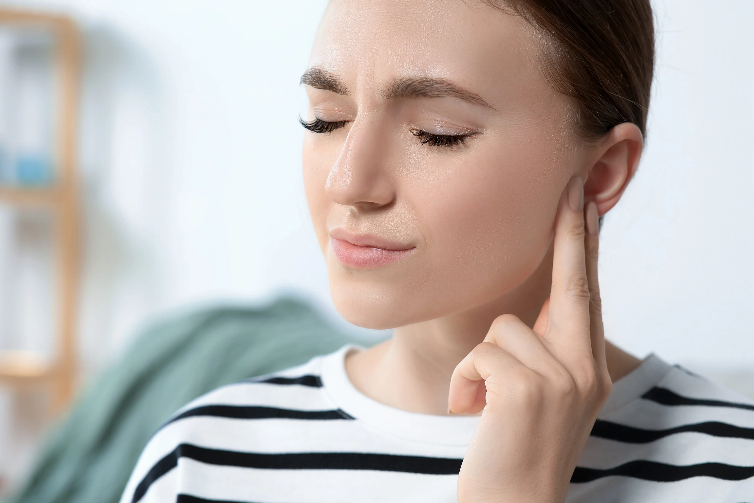 Frau hält sich ans Ohr, Ohrenschmerzen, Hörprobleme, Tinnitus im Alltag
